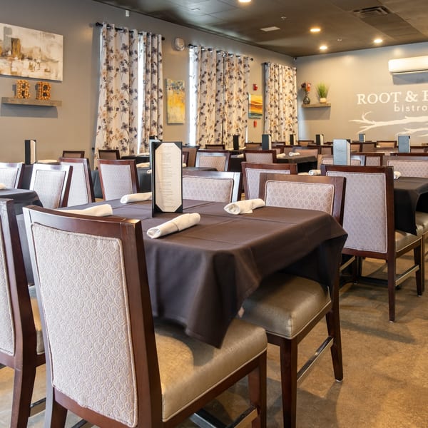 Interior of Root & Branch Bistro + Bar, featuring set tables with dark tablecloths and patterned chairs.