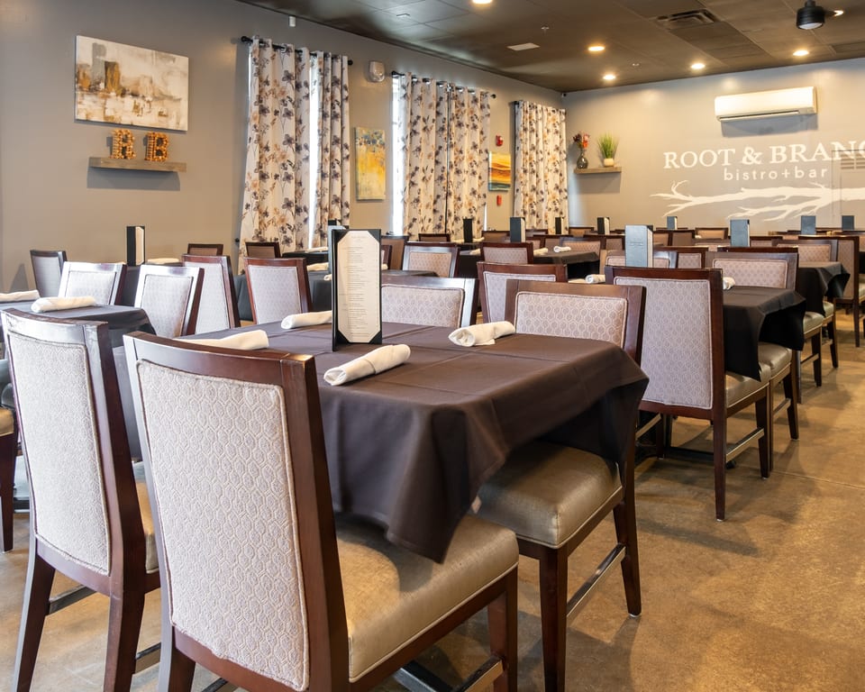 Interior of Root & Branch Bistro + Bar, featuring set tables with dark tablecloths and patterned chairs.