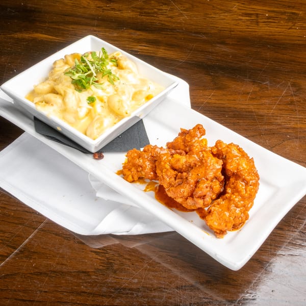 Mac and cheese with herbs and orange chicken on white plates, on a wooden table.