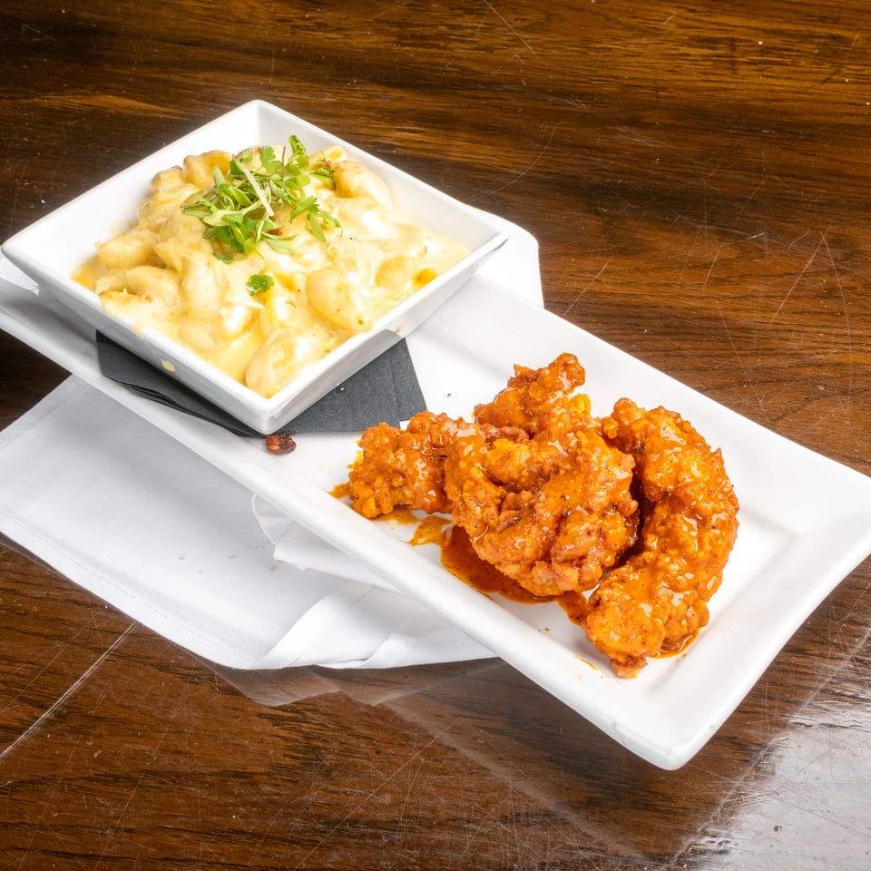 Mac and cheese with herbs and orange chicken on white plates, on a wooden table.