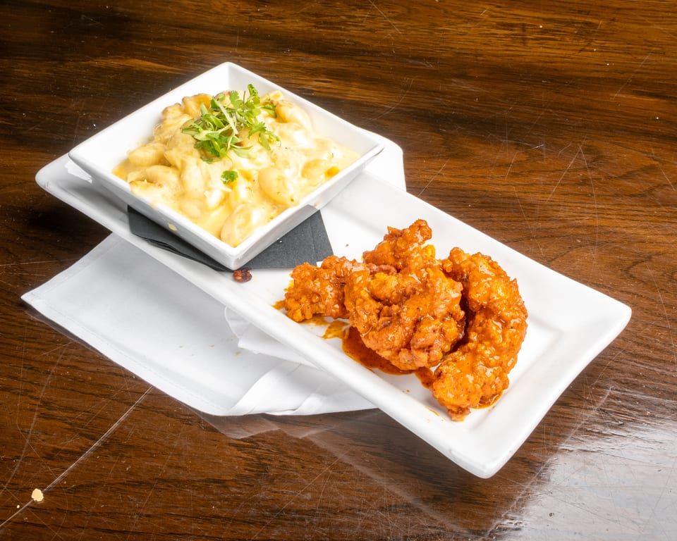 Mac and cheese with herbs and orange chicken on white plates, on a wooden table.