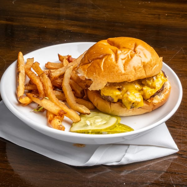 Cheeseburger with melted cheese, a side of golden fries, and pickle slices on a white plate.