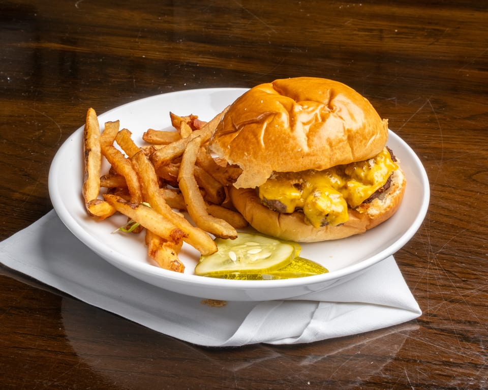 Cheeseburger with melted cheese, a side of golden fries, and pickle slices on a white plate.