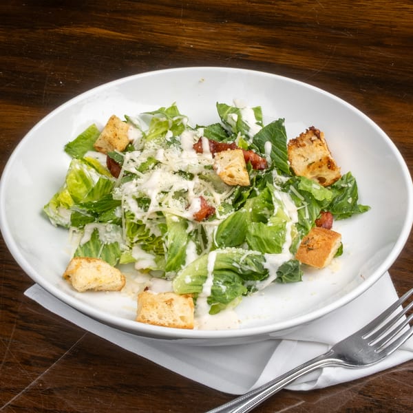 Caesar salad with romaine lettuce, croutons, bacon, and parmesan cheese in a white bowl.