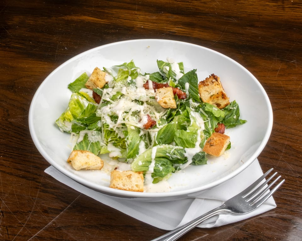 Caesar salad with romaine lettuce, croutons, bacon, and parmesan cheese in a white bowl.