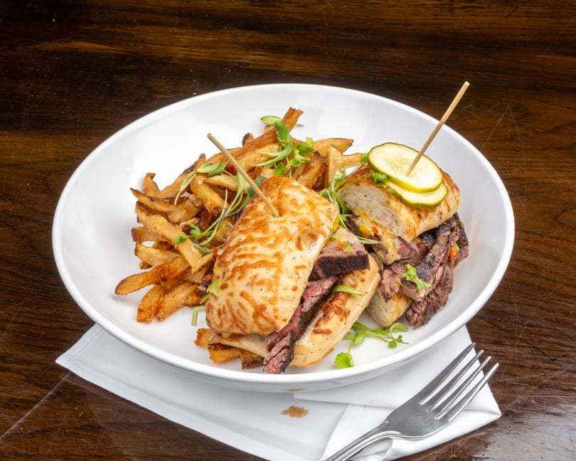 Grilled steak sandwich with melted cheese, pickles, and a side of golden french fries.