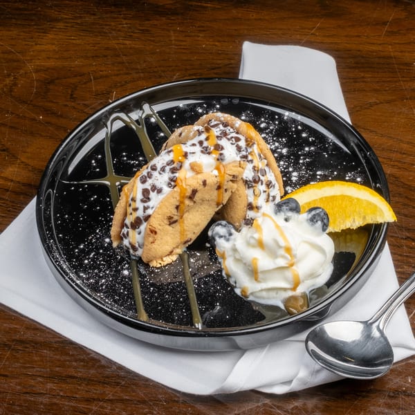 Two cookie tacos filled with ice cream, chocolate chips, caramel, whipped cream, blueberries, and orange.