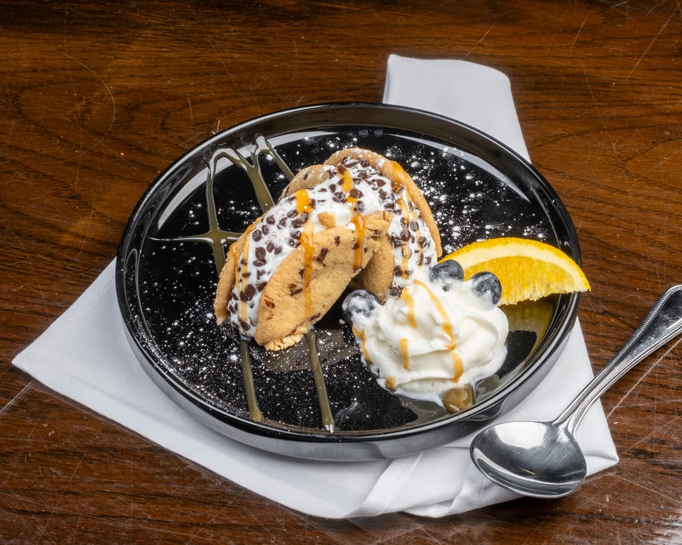 Two cookie tacos filled with ice cream, chocolate chips, caramel, whipped cream, blueberries, and orange.