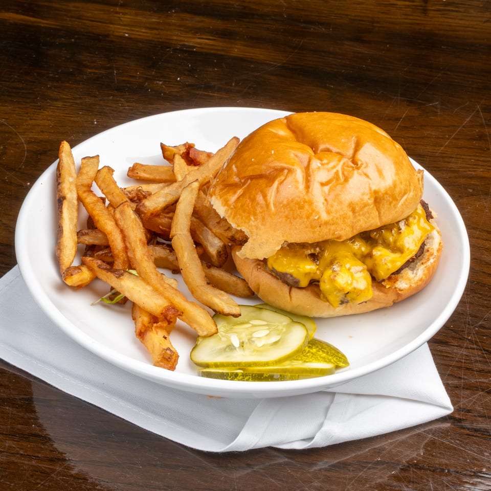 Cheeseburger with melted cheese, a side of fries, and pickle slices on a white plate.