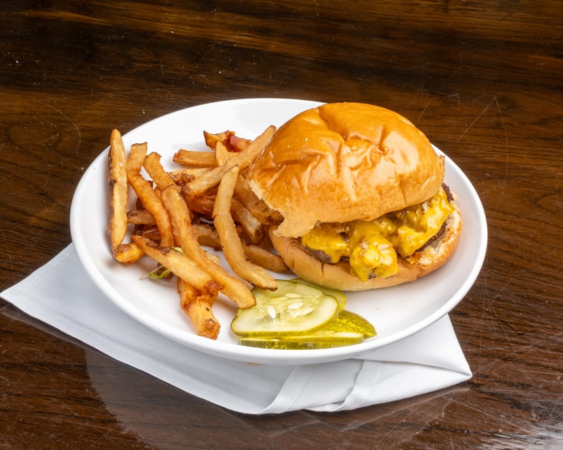 Cheeseburger with melted cheese, a side of fries, and pickle slices on a white plate.