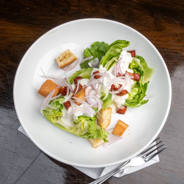 A Caesar salad with lettuce, bacon, red onions, croutons, and dressing in a white bowl.
