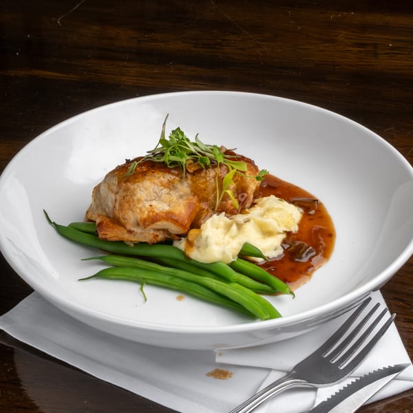 Savory pastry dish with mashed potatoes, green beans, and gravy in a white bowl on a wooden table.
