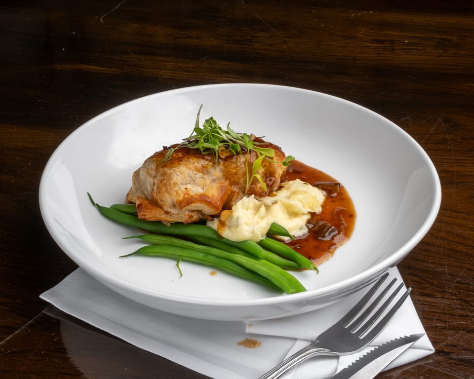 Savory pastry dish with mashed potatoes, green beans, and gravy in a white bowl on a wooden table.