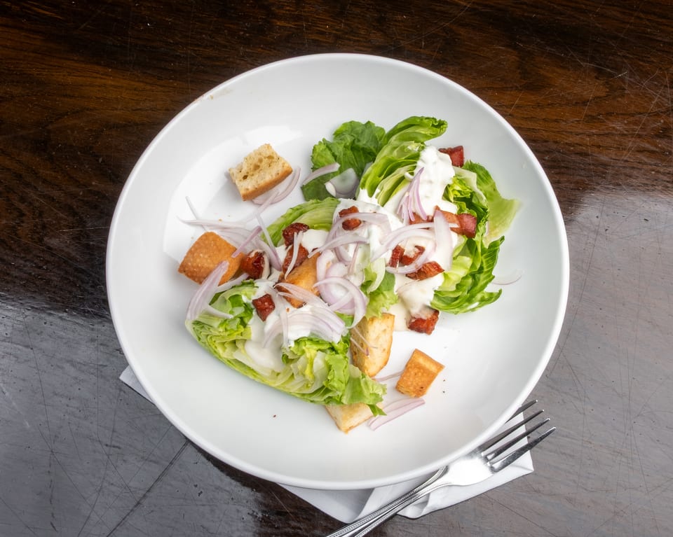 Caesar salad with lettuce, bacon, red onions, croutons, and dressing in a white bowl.