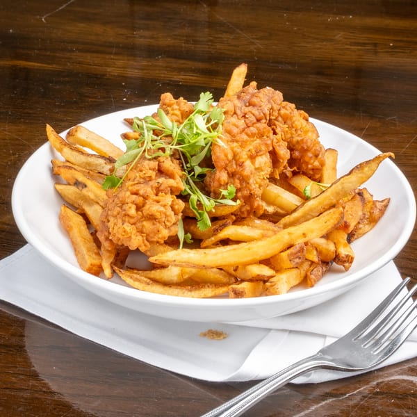 Crispy fried chicken tenders and golden french fries, garnished with fresh herbs, in a white bowl.