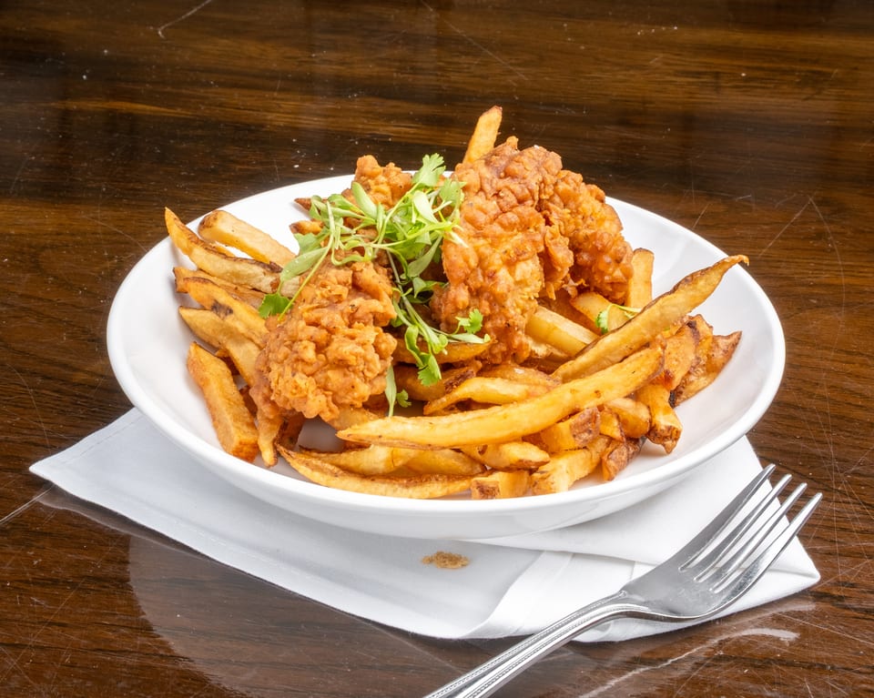 Crispy fried chicken tenders and golden french fries, garnished with fresh herbs, in a white bowl.