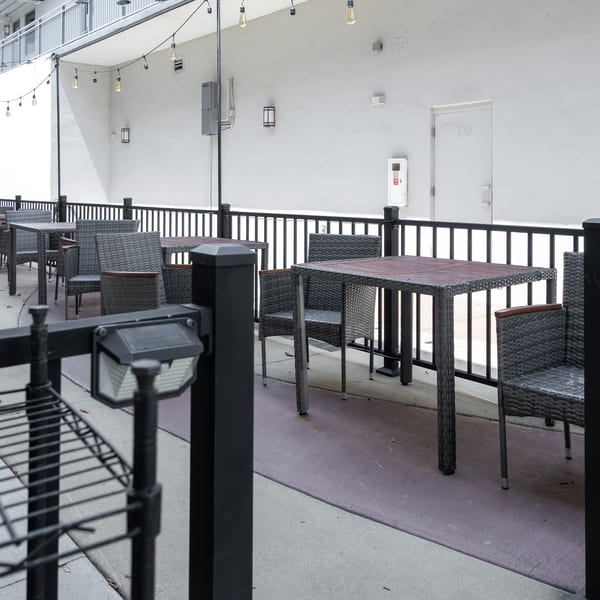 Outdoor patio with dark wicker chairs and tables, black railings, and string lights overhead.