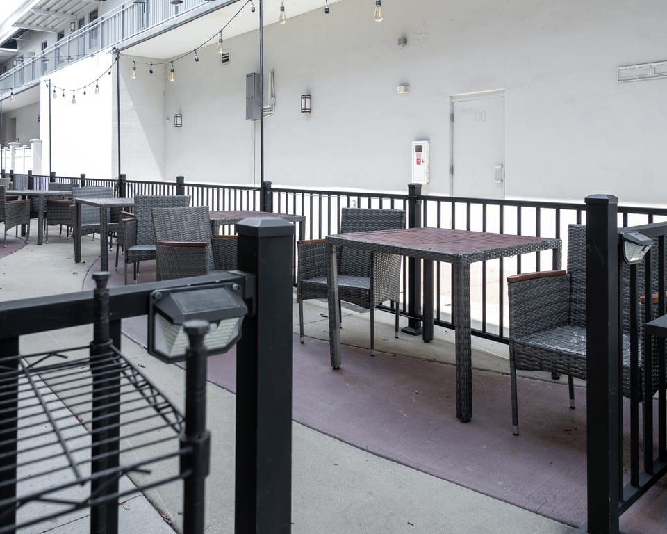Outdoor patio with dark wicker chairs and tables, black railings, and string lights overhead.