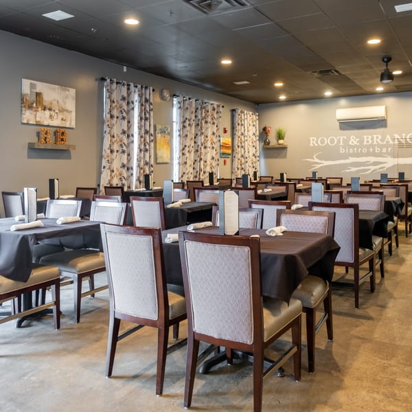 Interior of Root & Branch Bistro + Bar, showing rows of dining tables with dark tablecloths and upholstered chairs.