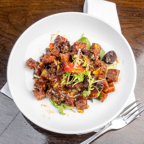 Sweet and sour pork belly with cilantro and red chili garnish on a white plate.
