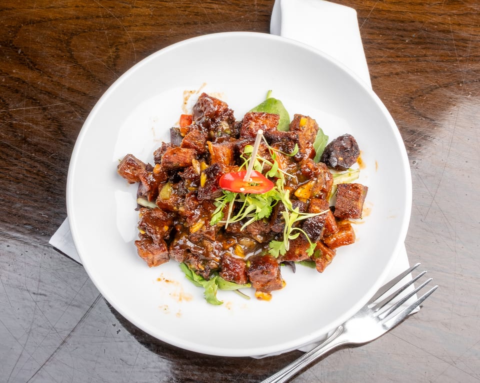 Sweet and sour pork belly with cilantro and red chili garnish on a white plate.